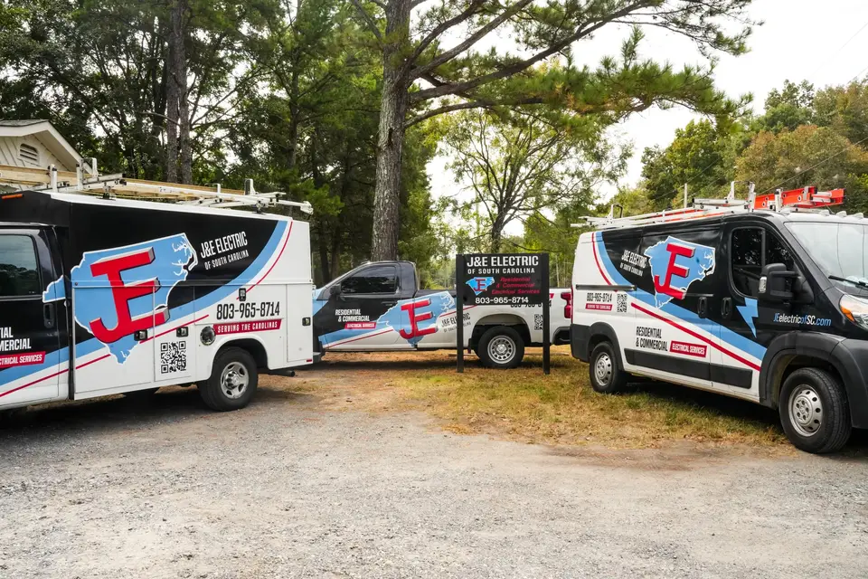Three J&E Electric of South Carolina service vehicles parked around the company sign.