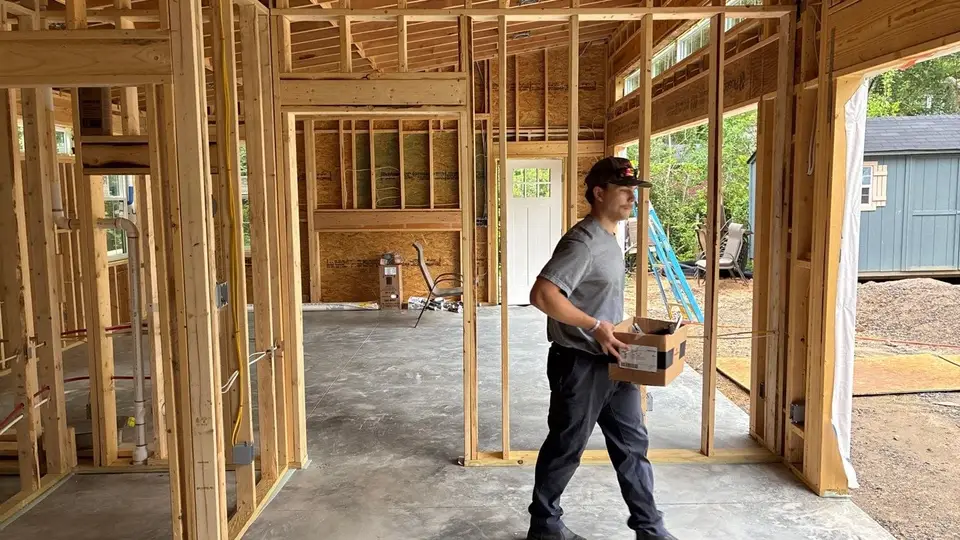 A J&E Electric electrician carrying materials through a framed house during rough-in.